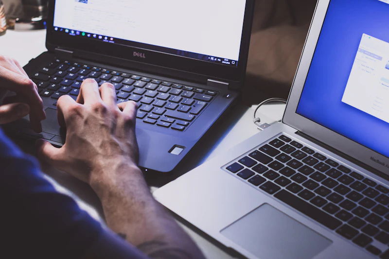 Hands working across two laptops